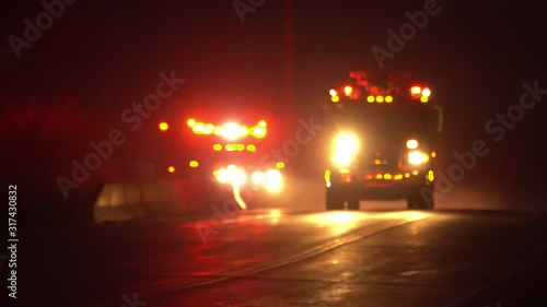 Emergency vehicles driving with lights flashing with ambulance following fire truck down road at night with sirens on.