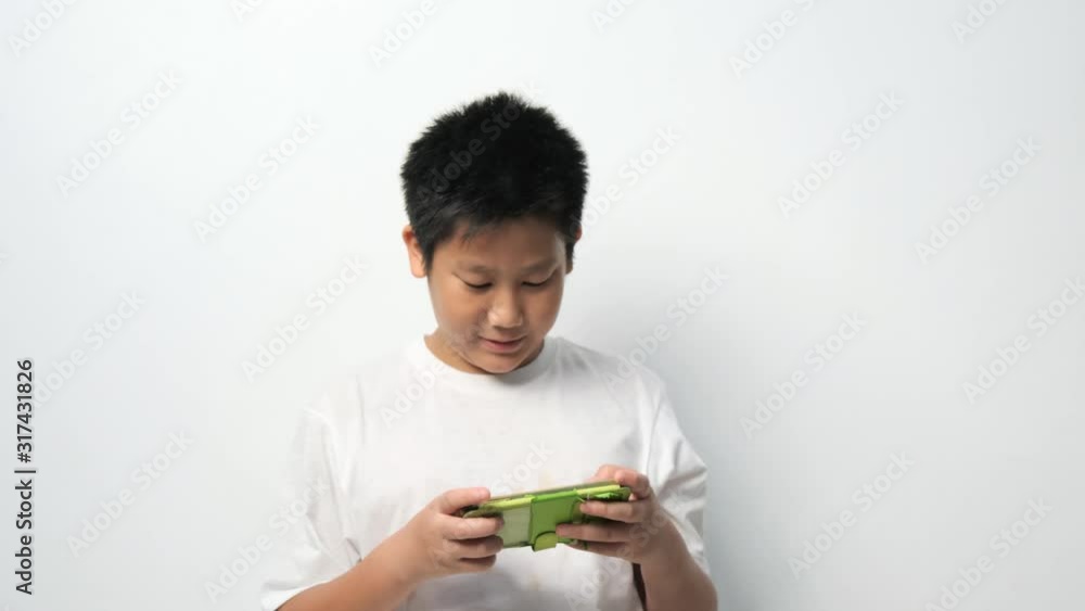Asian boy using smartphone playing game online with white wall. Asian boy using smartphone playing game online with white wall.