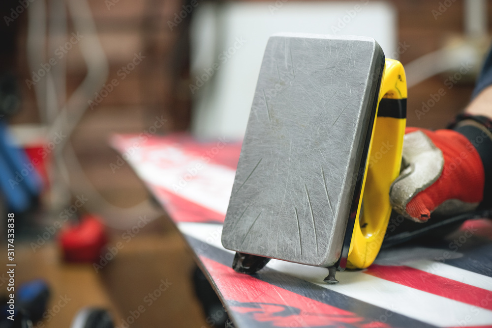 Fototapeta premium Worker is applying a wax on a slippery surface of snowboard by iron close up.