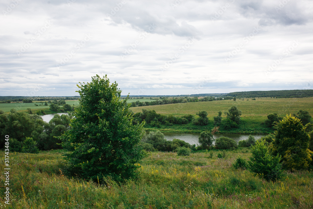 Path in a green field, panoramic view of the river in summer. View from the top of the hill