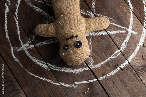 Voodoo doll on a wooden background with dramatic lighting. The concept of witchcraft and black art and the occult. Burlap doll on the background of a drawn star. Stuck pins in the doll. photo