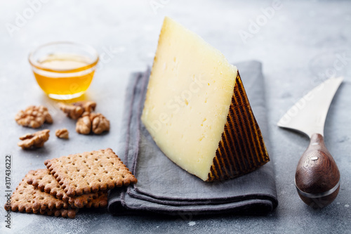 Hard cheese, Manchego with nuts, honey and crackers on grey background. Close up. photo