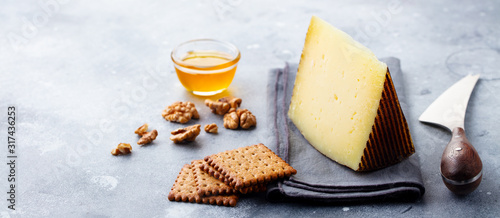 Hard cheese, Manchego with nuts, honey and crackers on grey background. Copy space. photo