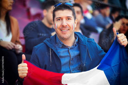 Happy french supporter holding national flag in hands at international football match