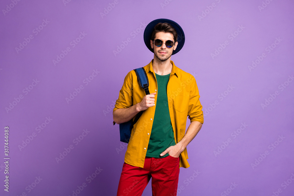 Portrait of gorgeous charismatic guy hold blue backpack stand isolated over violet color background wear stylish outfit velvet hat Portrait of gorgeous charismatic guy hold blue backpack stand isolated over violet color background wear stylish outfit velvet hat