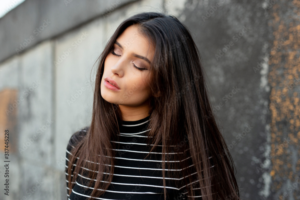 Beauty portrait of a sensual girl with straight brunette hair, dressed in modern clothes, with makeup, closed eyes, supported by a black wall. Beauty portrait of a sensual girl with straight brunette hair, dressed in modern clothes, with makeup, closed eyes, supported by a black wall.