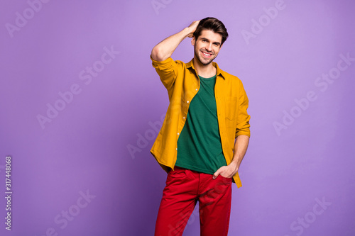 Photo of cheerful positive attractive handsome man smiling toothily in red pants isolated violet pastel color background combing his hair