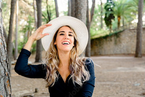 A young woman laughing with happiness posing fun in front of the camera with a hat.