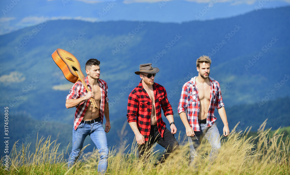 Enjoying freedom together. Long route. Group of young people in checkered shirts walking together on top of mountain. Men with guitar hiking on sunny day. Tourists hiking concept. Hiking with friends