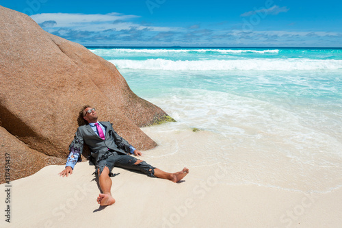 Survivor castaway businessman washed up on a tropical beach in a ragged torn suit photo
