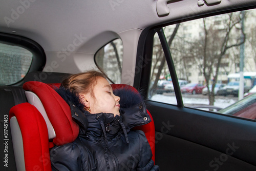 girl in blue warm clothes sits unbuckled in a car seat and sleeps