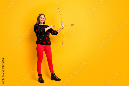 Full body profile photo of funny lady work as cupid hold bow arrow aiming feelings love couple wear hearts pattern pullover red trousers shoes isolated yellow color background
