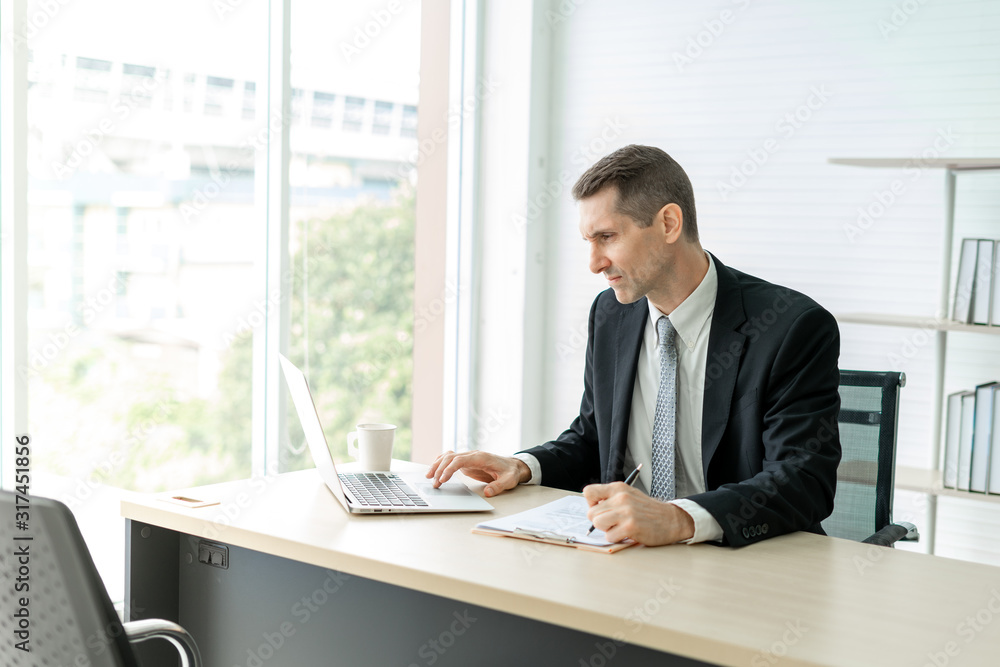 Stressed businessman looking and typing laptop on desk in working room at office Stressed businessman looking and typing laptop on desk in working room at office