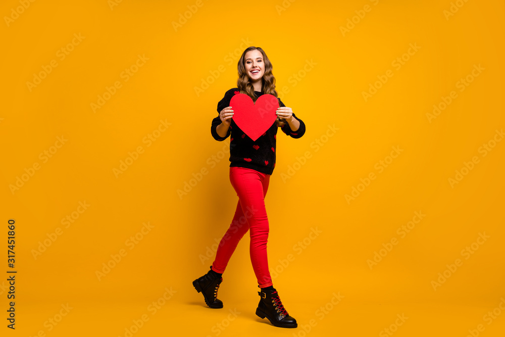 Full length photo of pretty lady hold big paper heart walk street creative idea date invitation for boyfriend wear hearts pattern sweater red pants shoes isolated yellow color background