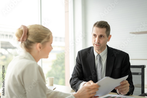 Boss businessman talking about report with woman employee at desk in office