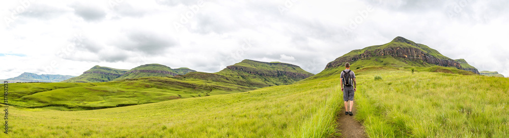 Man hiking on a small trail with a beautiful panorama of the green mountains of Maloti Drakensberg Park, Rainbow Gorge Trail, South Africa