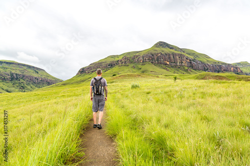 Man hiking on a small trail with a beautiful view to the green mountains of Maloti Drakensberg Park, Rainbow Gorge Trail, South Africa