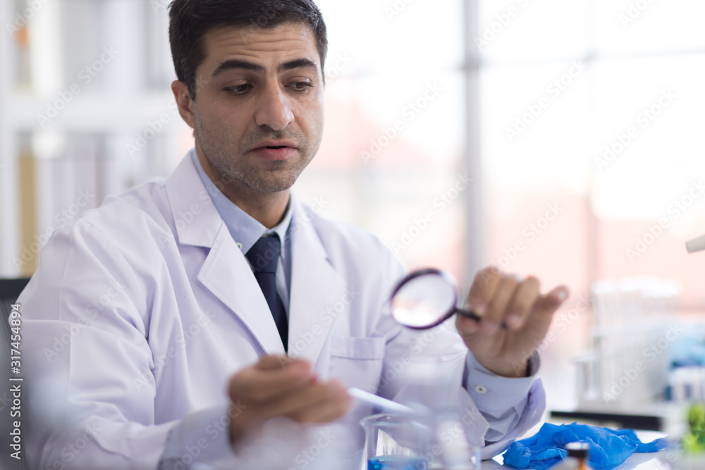 A male scientist with a magnifying glass looking at a science test tube in a research laboratory A male scientist with a magnifying glass looking at a science test tube in a research laboratory
