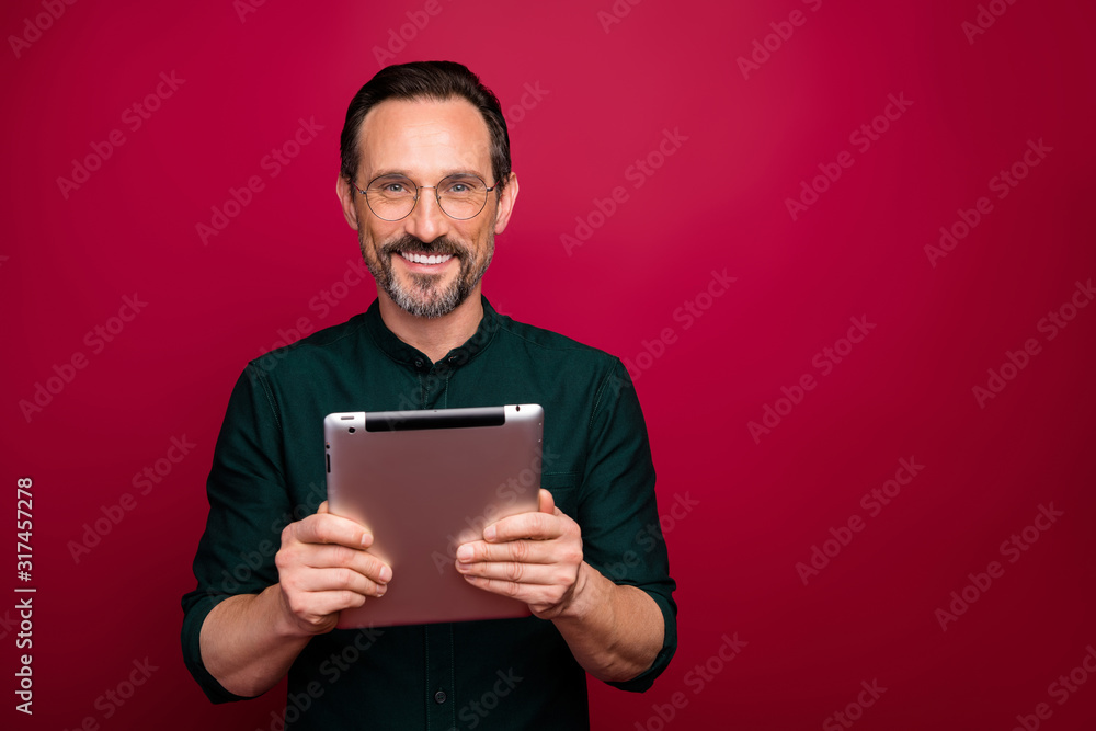 Photo of cheerful attractive man advertising new generation of gadgets standing near empty space smiling toothily isolated red vivid color background Photo of cheerful attractive man advertising new generation of gadgets standing near empty space smiling toothily isolated red vivid color background