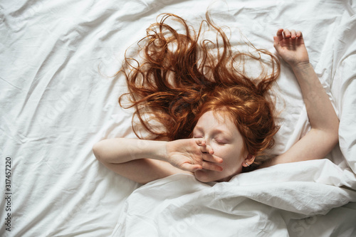 Red-haired little girl wakes up in the morning in her crib