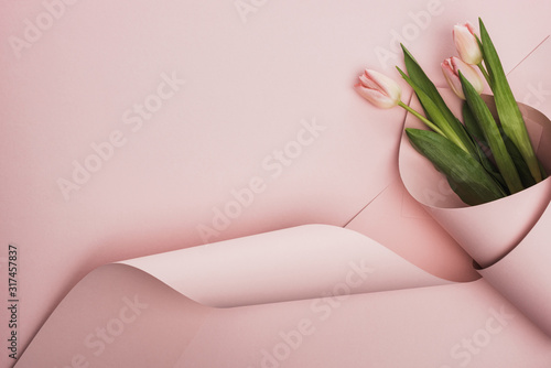 Top view of tulips wrapped in paper on pink background