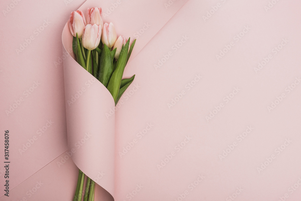Fototapeta premium widok z góry na bukiet tulipanów zawinięty w papier wirować na różowym tle