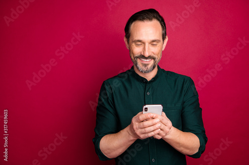 Close-up portrait of his he nice attractive cheerful cheery brown-haired man using digital gadget device isolated on bright vivid shine vibrant maroon burgundy marsala red color background © deagreez