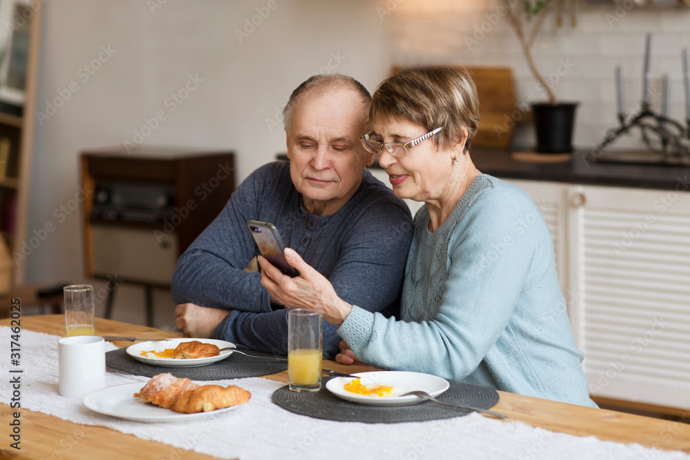 Senior couple eating breakfast and using smartphone at home Senior couple eating breakfast and using smartphone at home