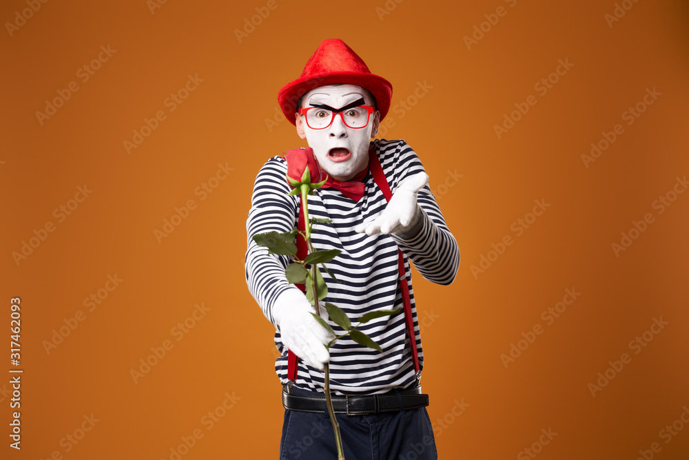 Sad mime man in red hat and vest with rose in hands on orange background Sad mime man in red hat and vest with rose in hands on orange background