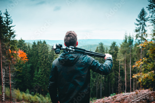 Fototapeta man with tripod and camera looking at a landscape