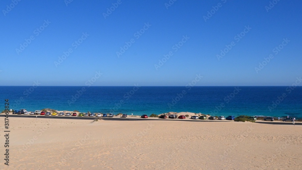 Cars parked on the side of the road next to the sand dunes at Parque Natural de Corralejo at Fuerteventura, Canary Islands, Spain. Parking space on the coast. Panoramic view