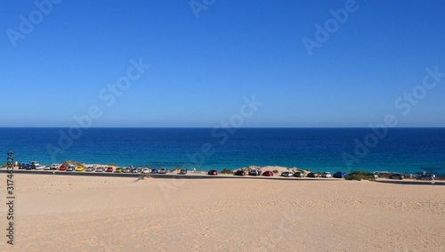 Cars parked on the side of the road next to the sand dunes at Parque Natural de Corralejo at Fuerteventura  Canary Islands  Spain. Parking space on the coast. Panoramic view