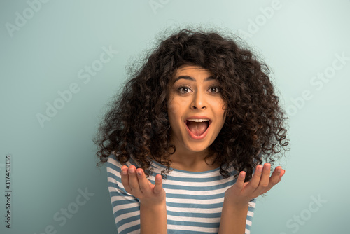 irritated mixed race girl shouting at camera and showing indignation gesture on grey background