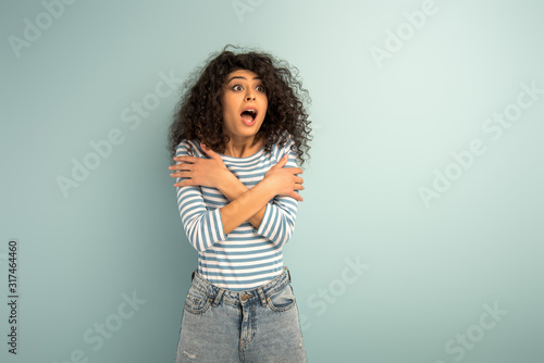 scared bi-racial girl hugging herself with hands while looking away on grey background