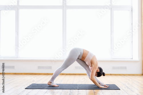 Charming flexible slim girl fitness model doing one sided fold exercise parsvottanasana Pyramid pose standing on rug on floor in spacious gym. Concept of regular yoga and pilates. Advertising space