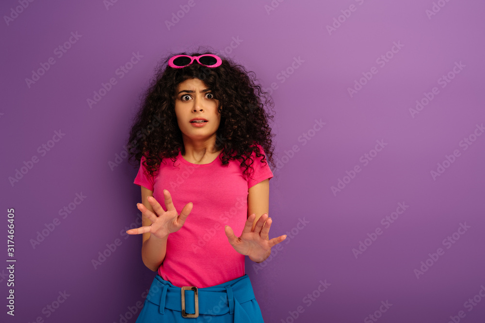 scared bi-racial girl showing stop gesture while looking at camera on purple background scared bi-racial girl showing stop gesture while looking at camera on purple background
