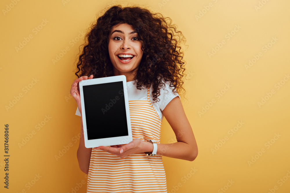 cheerful bi-racial girl showing digital tablet with blank screen on yellow background cheerful bi-racial girl showing digital tablet with blank screen on yellow background