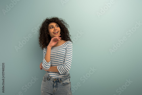 happy bi-racial girl smiling while looking away on grey background