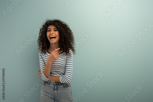 excited bi-racial girl laughing while pointing with finger on grey background