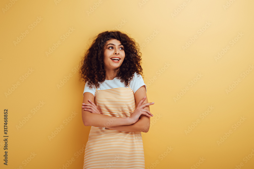 smiling, dreamy bi-racial girl standing with crossed arms and looking away on yellow background smiling, dreamy bi-racial girl standing with crossed arms and looking away on yellow background