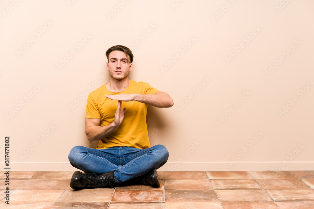 Young caucasian man sitting on the floor isolated showing a timeout gesture.