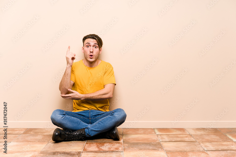 Young caucasian man sitting on the floor isolated having some great idea, concept of creativity. Young caucasian man sitting on the floor isolated having some great idea, concept of creativity.