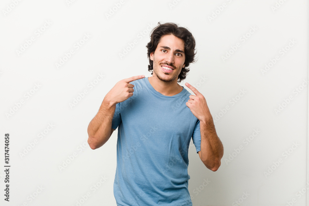 Young handsome man against a white background smiles, pointing fingers at mouth. Young handsome man against a white background smiles, pointing fingers at mouth.
