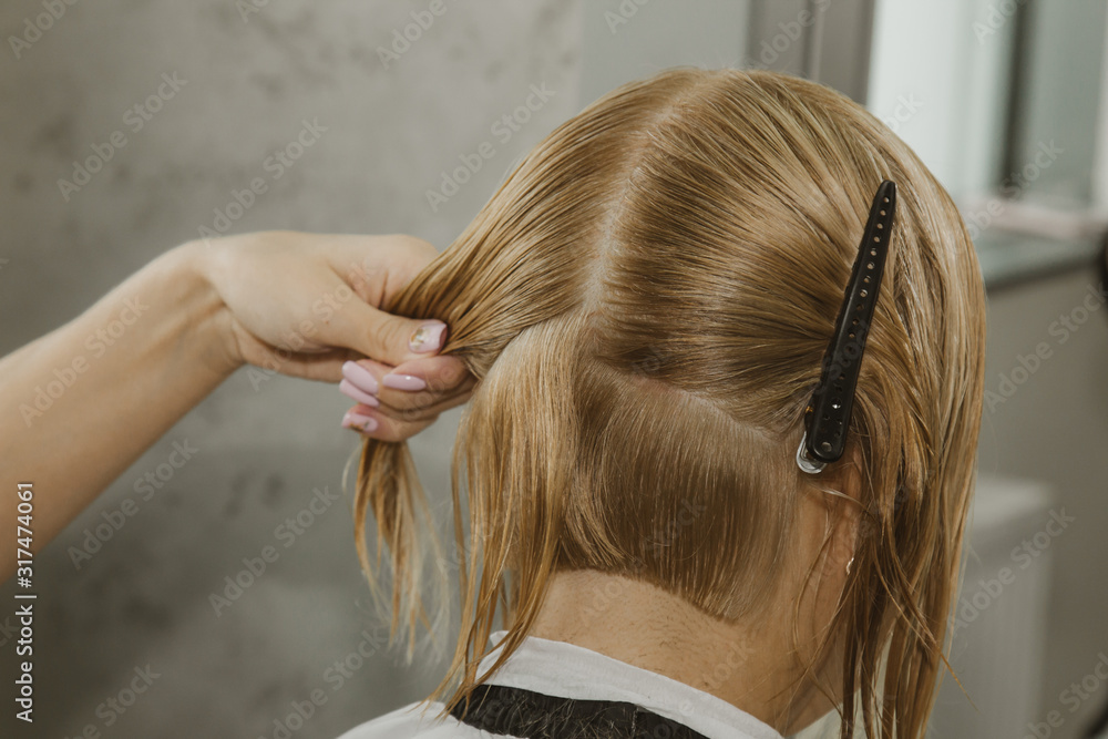 Fototapeta premium Woman with medium long blonde hair. With a short haircut at the hairdresser at the stylist using scissors. Care procedures. The master shortens his hair.