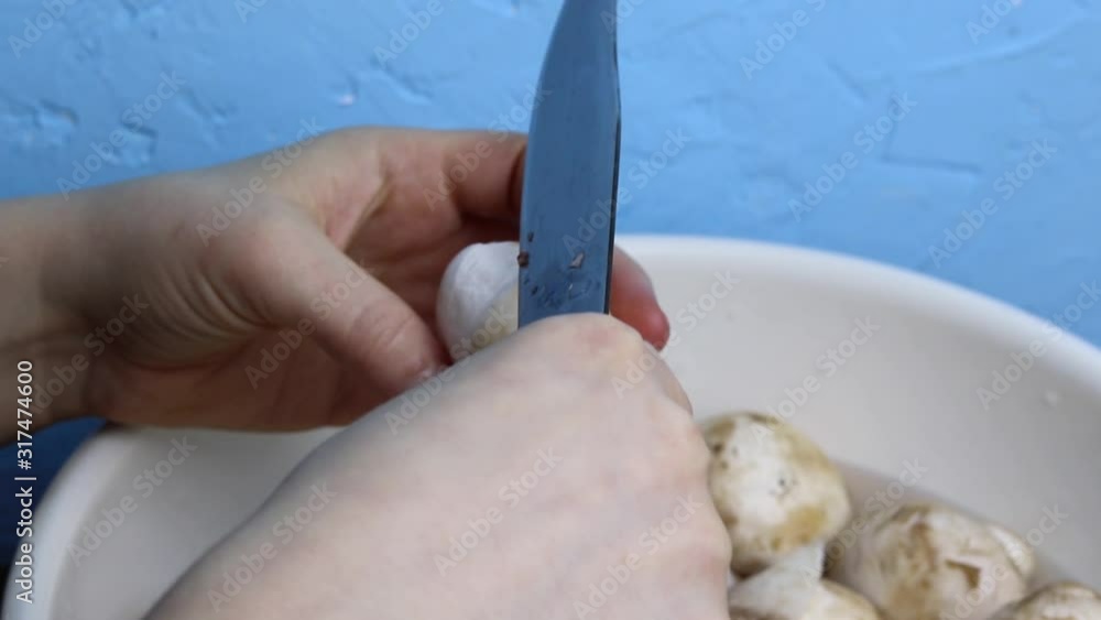 Female hands brush a mushroom with a knife in an enameled white bowl. Copy space - concept of cleaning vegetables from dirt, cooking ingredients for the dish. Female hands brush a mushroom with a knife in an enameled white bowl. Copy space - concept of cleaning vegetables from dirt, cooking ingredients for the dish.