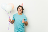 Young man celebrating a party holding balloons smiling and raising thumb up
