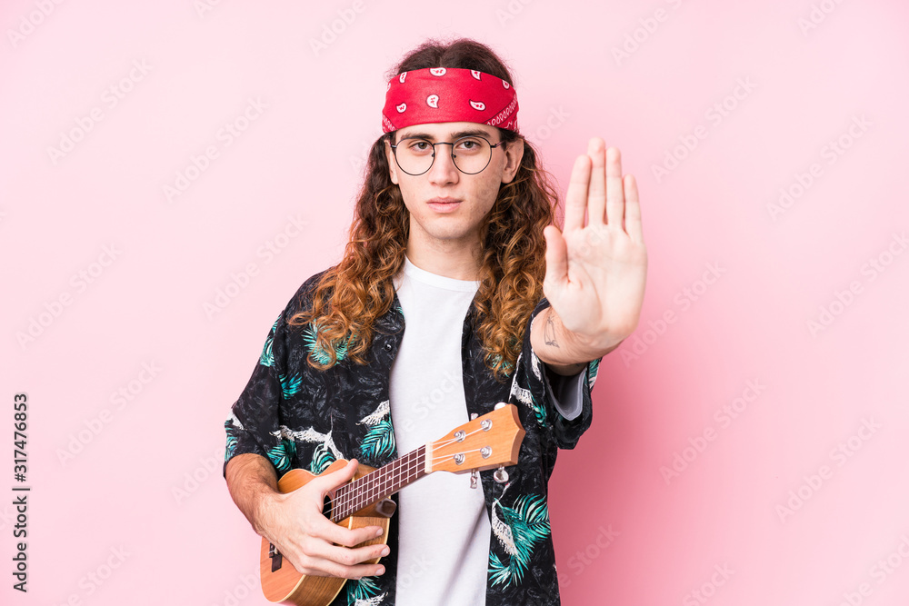 Long hair hippie man holding a ukelele isolated standing with outstretched hand showing stop sign, preventing you.