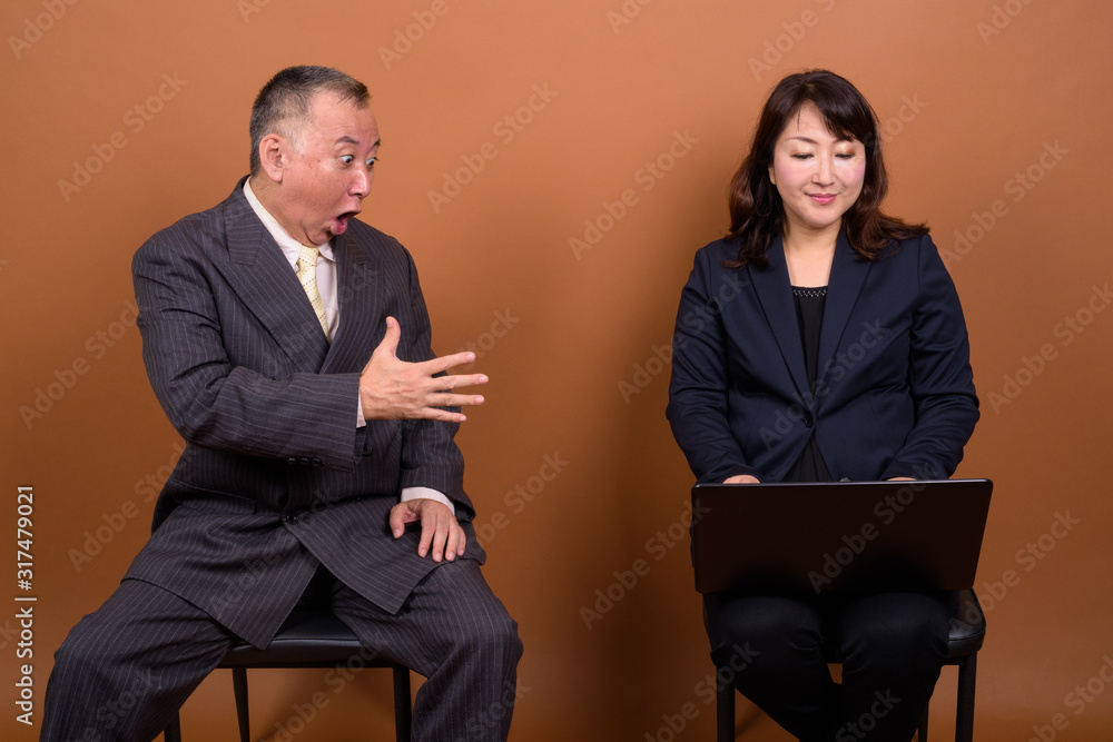 Obraz premium Mature Asian businessman with mature Asian businesswoman using laptop