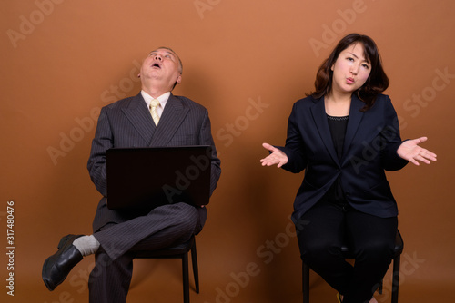 Mature Asian businesswoman with mature Asian businessman using laptop