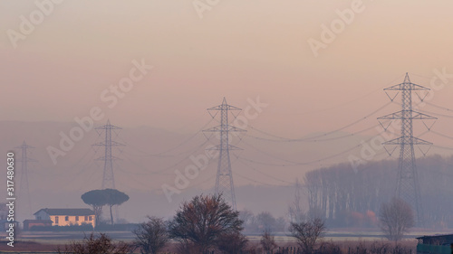 Electric pylons covered in fog and smog shortly after the dawn of a new day